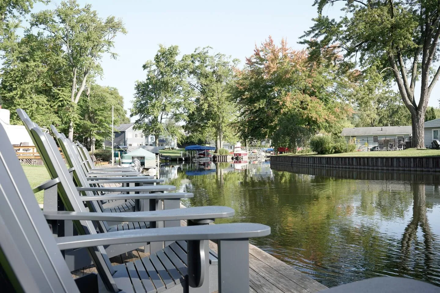 A row of gray Adirondack chairs on a dock looking down a calm channel